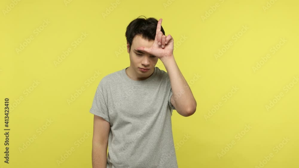 Frustrated unlucky young man in gray t-shirt standing showing loser gesture, upset about dismissal, lost job, failure in relations, life difficulties. Indoor studio shot isolated on yellow background Frustrated unlucky young man in gray t-shirt standing showing loser gesture, upset about dismissal, lost job, failure in relations, life difficulties. Indoor studio shot isolated on yellow background