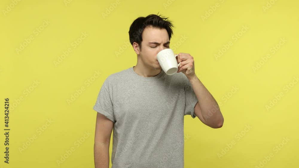 Young man in casual gray t-shirt drinking hot or cold beverage and feeling unpleasant sore pain in teeth or gums, sensitivity, dental problems. Indoor studio shot isolated on yellow background Young man in casual gray t-shirt drinking hot or cold beverage and feeling unpleasant sore pain in teeth or gums, sensitivity, dental problems. Indoor studio shot isolated on yellow background