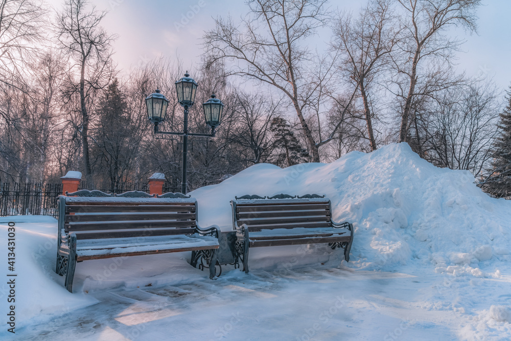 Two retro benches and a lantern near a large snowdrift at sunset in winter. A romantic meeting place. Trees and pure white snow, blue sky with pink sunset colors 