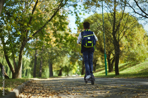 Schoolboy with backpack riding on electric scooter to school