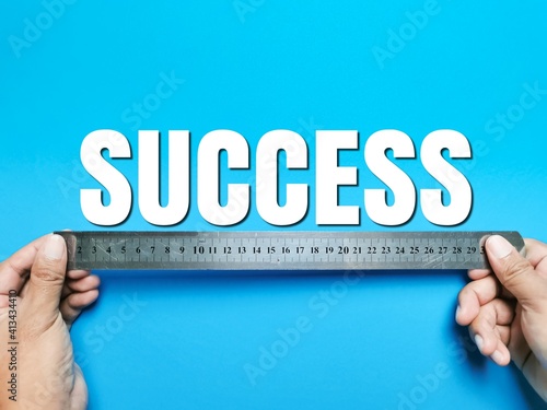 Top view text SUCCESS made from square letter tiles with hands holding metal ruler isolated on blue background. Business concept.