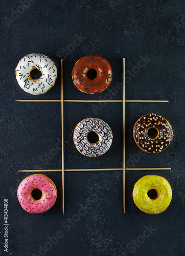 Multicolored donuts with glaze and splashes on a black background tic-tac-toe game
