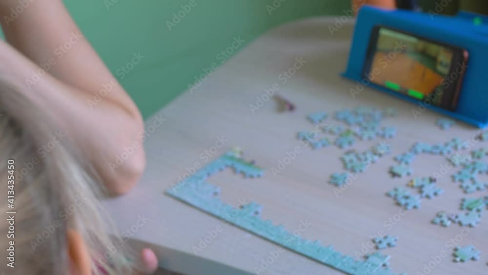 There is a mosaic on the table, next to it is a blue stand with a switched on smartphone. The favorite game of basketball teams is on the screen. The girl is watching the game. Back view There is a mosaic on the table, next to it is a blue stand with a switched on smartphone. The favorite game of basketball teams is on the screen. The girl is watching the game. Back view