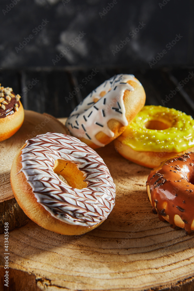 Multicolored donuts with glaze and sprinkles on wooden coasters on a black background