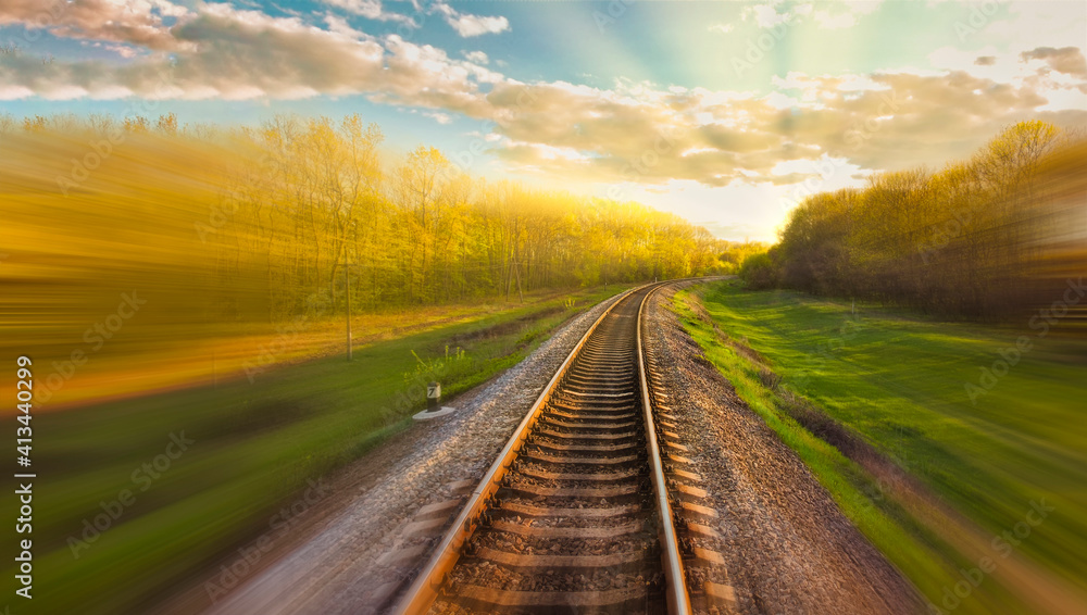 Railway track with motion blur effect. Blurred railway. Industrial conceptual landscape with blurred railway tracks and nature around. Blue sky with colorful clouds and sun. Railway.