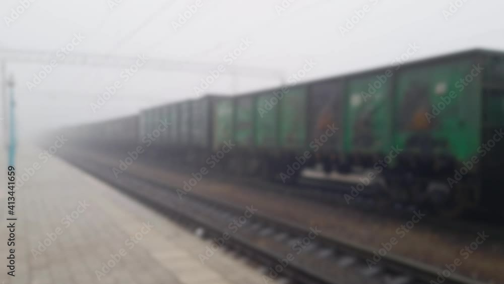 Cargo Train Moving On Platform Freight in foggy day. Train Passing Through Station. Wagons Rides On Steel Railway at mist. Heavy Industry Transportation Concept. Blurred defocused footage. Cargo Train Moving On Platform Freight in foggy day. Train Passing Through Station. Wagons Rides On Steel Railway at mist. Heavy Industry Transportation Concept. Blurred defocused footage.