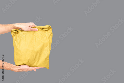 Close up female holds in hand brown clear empty blank craft paper bag for takeaway Delivery service concept. Copy space. Trendy colors 2021 - Gray and Yellow.