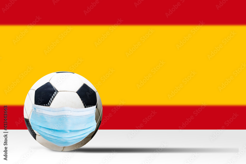 Soccer ball in a medical mask against the background of the flag of spain. Corona protection against viruses bacteria stop. Cancellation of sporting events. Copy space Soccer ball in a medical mask against the background of the flag of spain. Corona protection against viruses bacteria stop. Cancellation of sporting events. Copy space