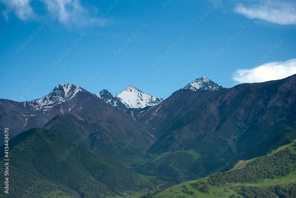 Mountain landscape of Kyrgyzstan. Among green valleys, mountains are visible at middle of the day. Tien Shan Mountains, Kyrgyzstan.