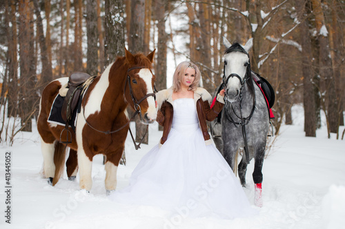 blond woman between horses outdoors in winter nature park. Portrait of a laughing woman with two horses. Friendship and pets concept.