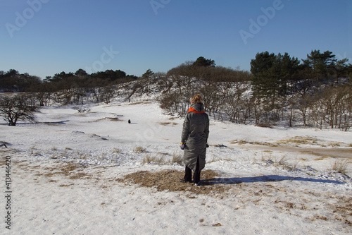 Woman on Dutch sand dunes looking to a playing child in the distance in the snow in winter. Near the village of Bergen. Called: Drie Banken, Russengat. Netherlands, February. photo