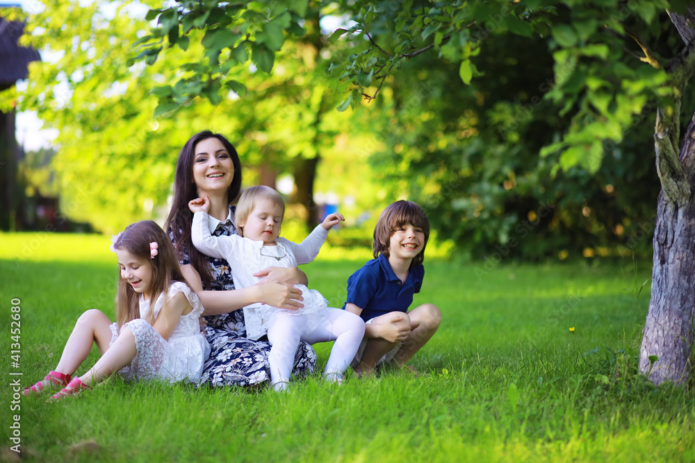 Young large family on a summer morning walk. Beautiful mother with children is playing in the park.