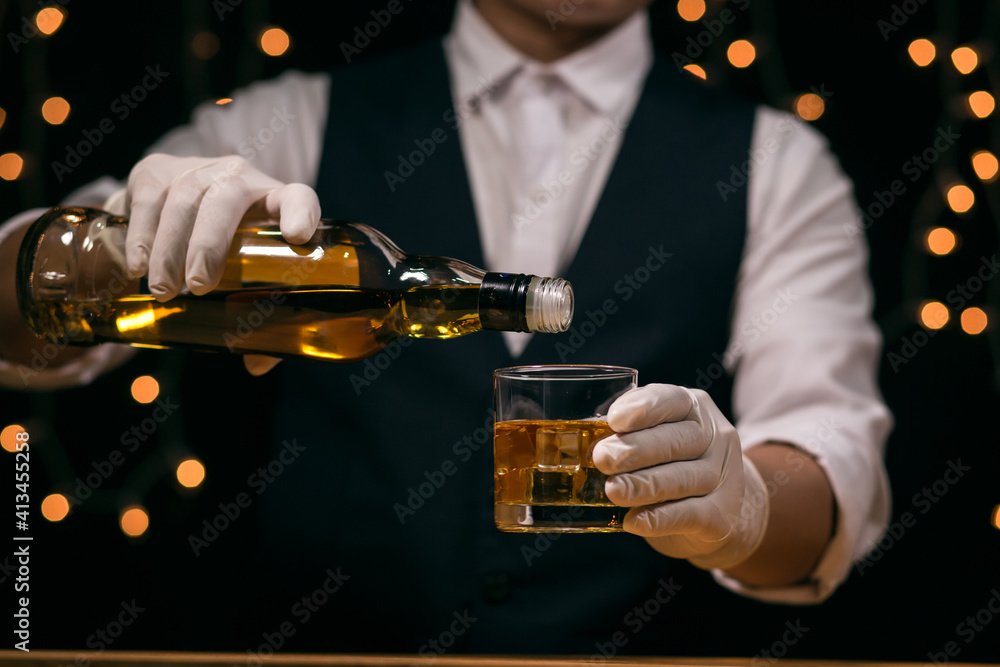 Waitress man standing pours whiskey into a glass Waitress man standing pours whiskey into a glass