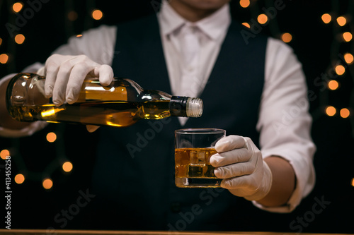 Waitress man standing pours whiskey into a glass 