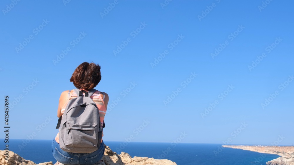 Fototapeta premium Girl tourist with a backpack on the background of the sky, back view