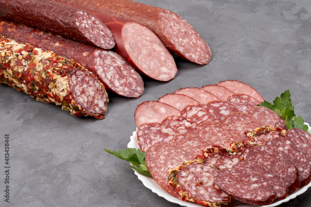 Set of jerky and uncooked smoked sausage whole and slices on a gray background, side view with copy space. Set of jerky and uncooked smoked sausage whole and slices on a gray background, side view with copy space.