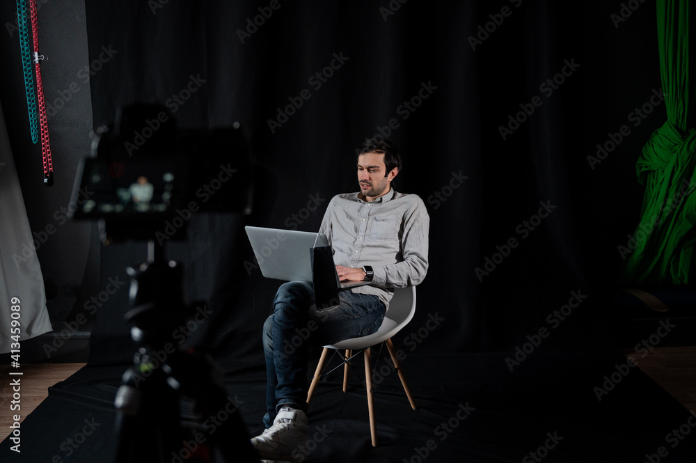 Man with laptop records video on camera in studio. Male vlogger in studio Man with laptop records video on camera in studio. Male vlogger in studio