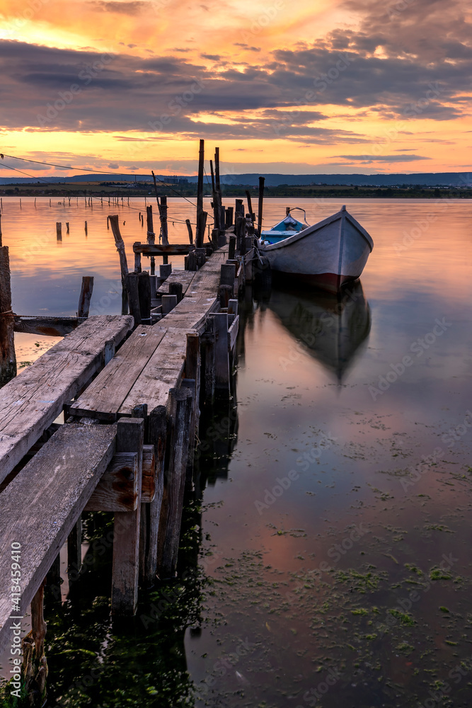 Amazing mood sunset at a lake coast with a boat at a wooden pier. Vertical view