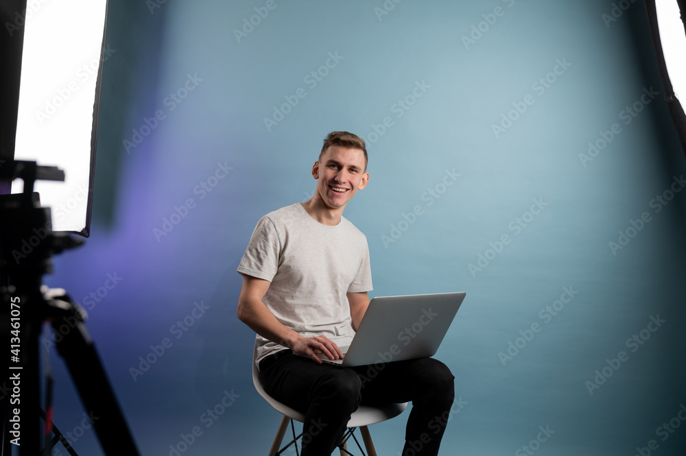 Young man using laptop indoors on blue background. Young caucasian man working on laptop