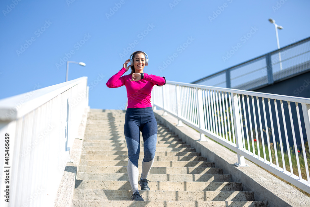 Young happy fitness woman in sportswear listen music on headphones and exercise outdoor