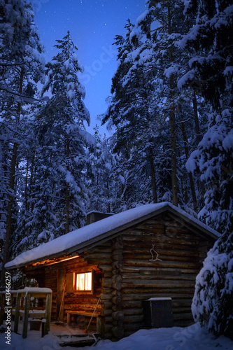 A log cabin in the winter night and stars in the night sky.
