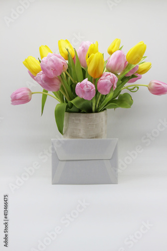 Fototapeta Naklejka Na Ścianę i Meble -  bouquet of pink and yellow tulips in a white vase,  envelope nearby