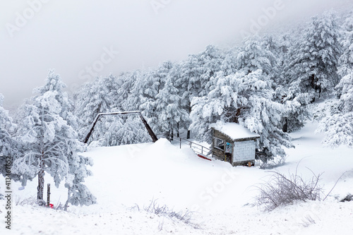 Zona de montaña nevada con caseta y árboles blancos.