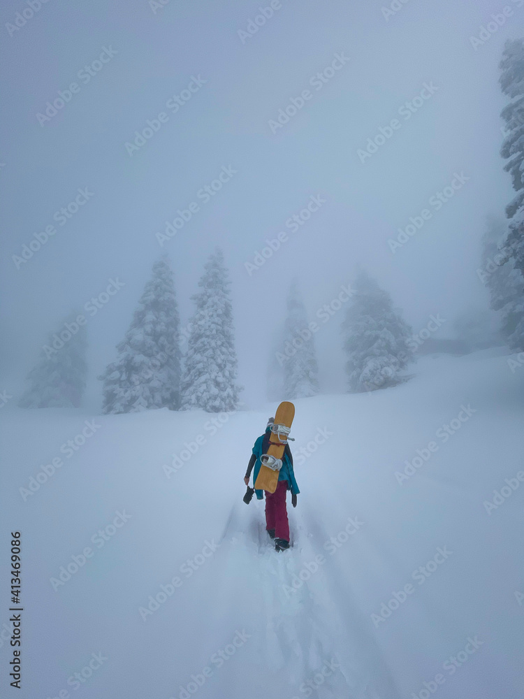 VERTICAL: Young female snowboarder hikes up a hill covered in fresh powder snow. VERTICAL: Young female snowboarder hikes up a hill covered in fresh powder snow.