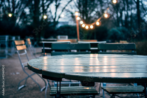 empty wooden chairs and tables in garden under electric light bulbs