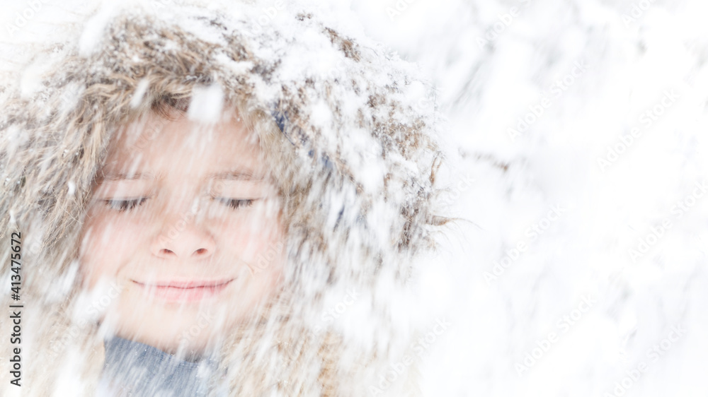 Happy child face close up. closed eyes smiling and happy with lots of blurred snow falling in front in winter covered in white hoarfrost. Winter is here fun kids outdoor activities banner. Copy space Happy child face close up. closed eyes smiling and happy with lots of blurred snow falling in front in winter covered in white hoarfrost. Winter is here fun kids outdoor activities banner. Copy space
