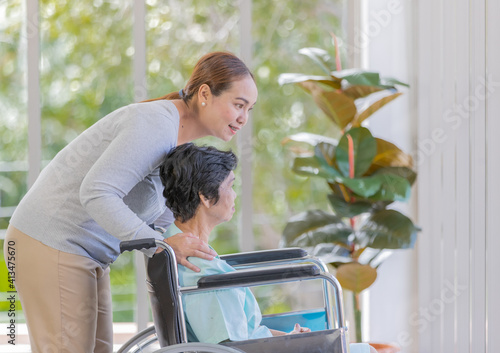 Asian woman's daughter take care of her senior old mother patient in wheelchair and support her with love and care photo