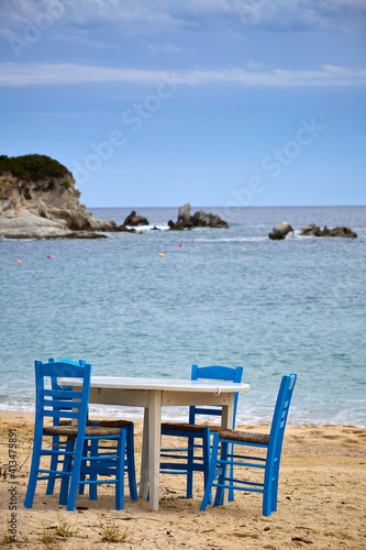 Table with traditional blue chairs at a sandy beach on Sythonia Peninsula, Greece