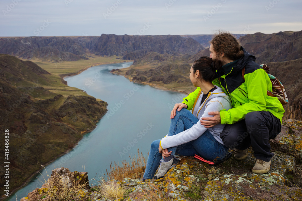 Young couple outdoors near the beautiful river canyon. Young people are resting on the edge of the cliff. Spring landscape. The Ili River. Kazakhstan