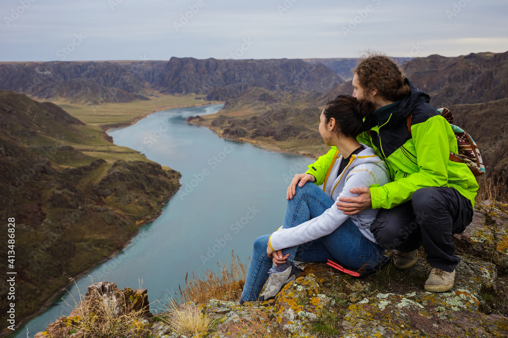 Fototapeta premium Young couple outdoors near the beautiful river canyon. Young people are resting on the edge of the cliff. Spring landscape. The Ili River. Kazakhstan