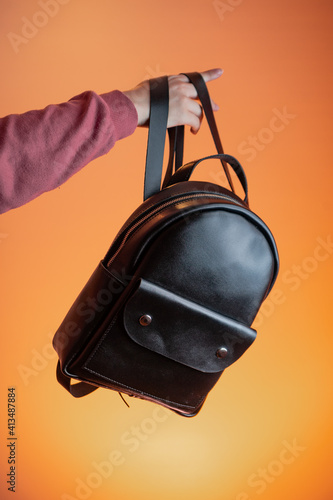 A woman's hand holds a leather backpack against an orange background