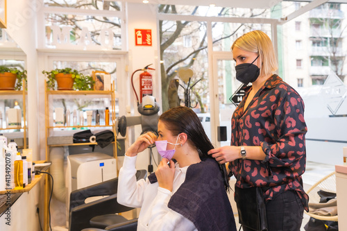 Hairdresser with face protection mask and the client putting on the mask. Security measures in the Covid-19 pandemic
