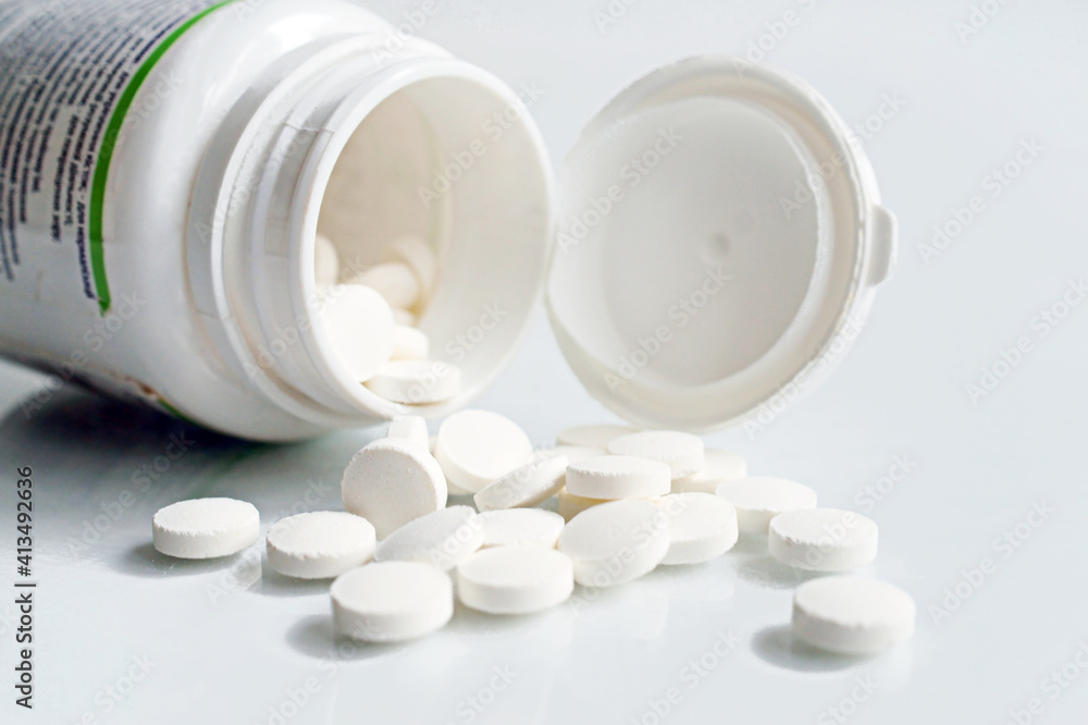 White pills and plastic bottle on white desktop.