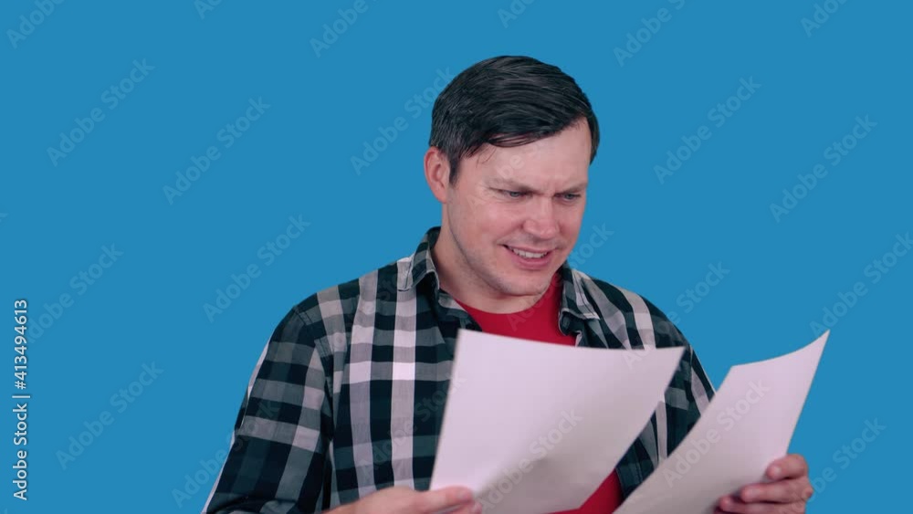 Joyful man looks at paper with documents, reading document, on blue background. Joyful man looks at paper with documents, reading document, on blue background.