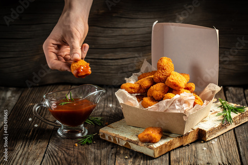 hands holdin chicken nuggets in ketchup in paper box on a wooden background. American food concept. fast food meal. banner, menu, recipe, place for text photo