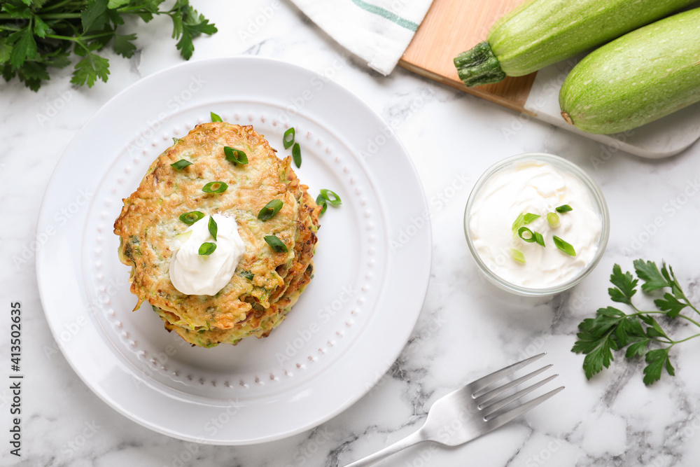 Delicious zucchini fritters served on white marble table, flat lay