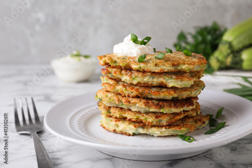 Delicious zucchini fritters with sour cream served on white marble table, closeup