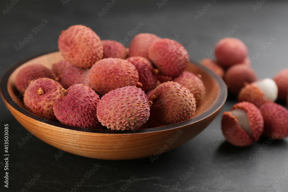 Fresh ripe lychee fruits in wooden bowl on black table Fresh ripe lychee fruits in wooden bowl on black table