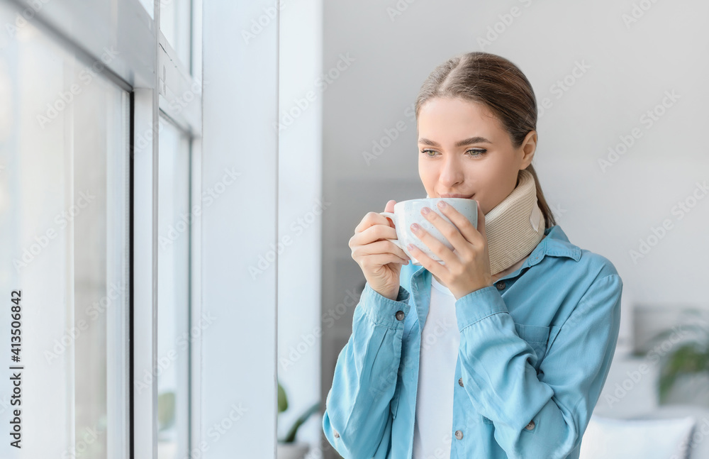 Young woman with cervical collar on neck drinking tea at home Young woman with cervical collar on neck drinking tea at home