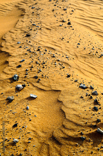 Gros Plan sur des petits cailloux gris posés à la surface du sable doré dans le désert.