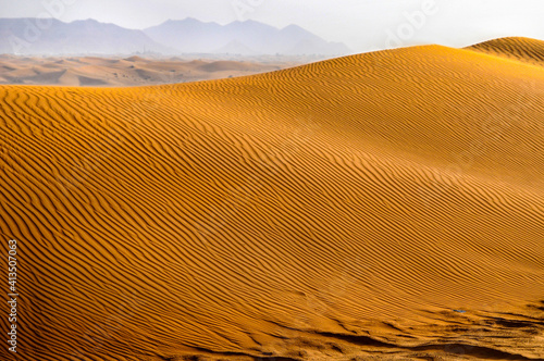 Vue sur une dune de sable doré dans le désert avec des montagnes en arrière-plan.
