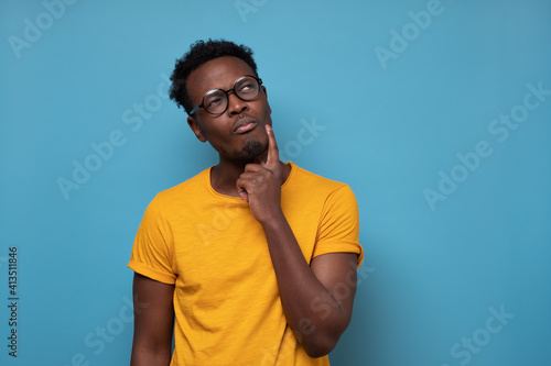 Young african man in glasses thinking over blue background. Studio shot photo