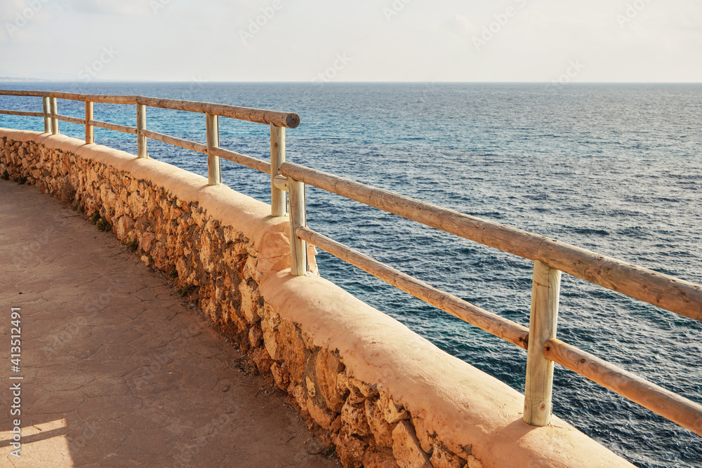 Obraz premium Stone road with wooden fence by sea cliff lit by morning sun