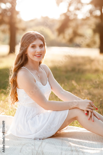 Young beautiful blonde woman with long hair in white dress in nature. Spends the weekend outside the city, outdoors, a picnic in the park in the meadow. relaxation in summer time