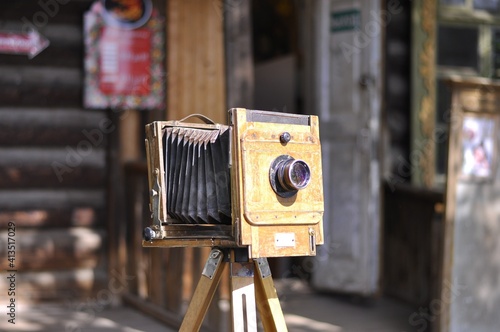 Vintage camera on a tripod on the background of an old wooden hut. A camera from the late 19th or early 20th century.  photo