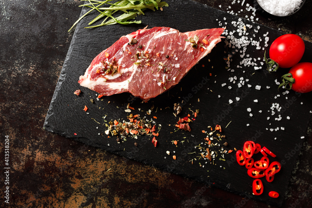 raw pork with spices for cooking on a fire or oven on a dark stone background